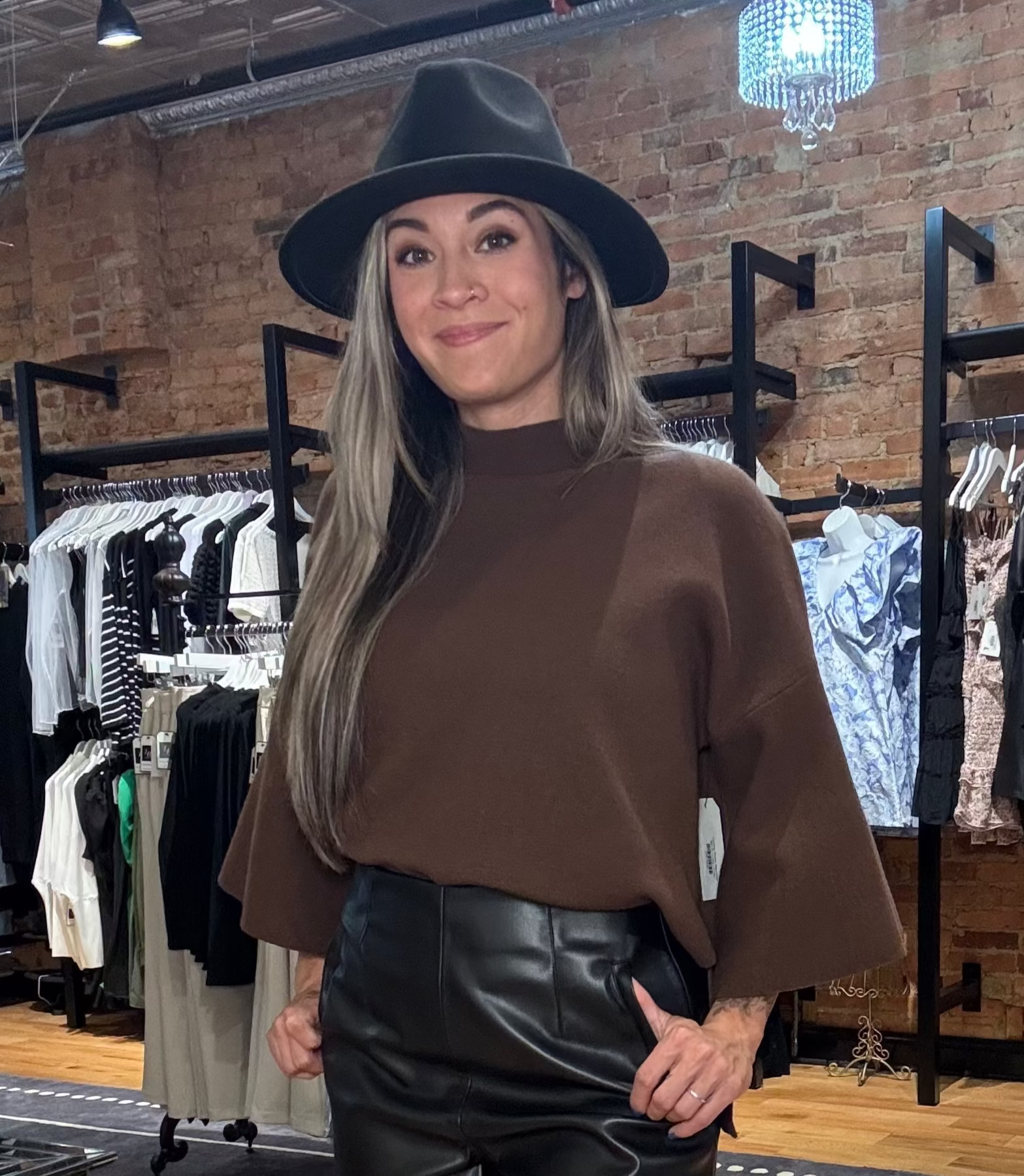Woman in a clothing store wearing a brown sweater, black leather shorts, and tan boots.