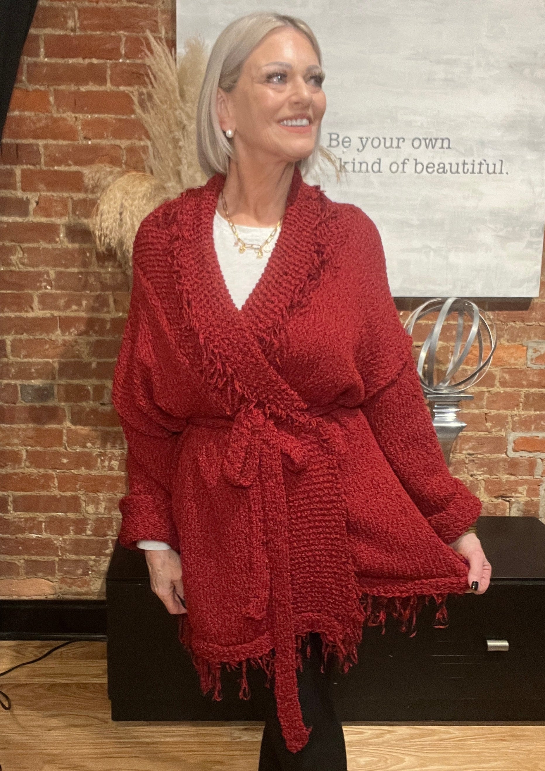 Person wearing a red knitted cardigan in front of a brick wall with a magazine on top.