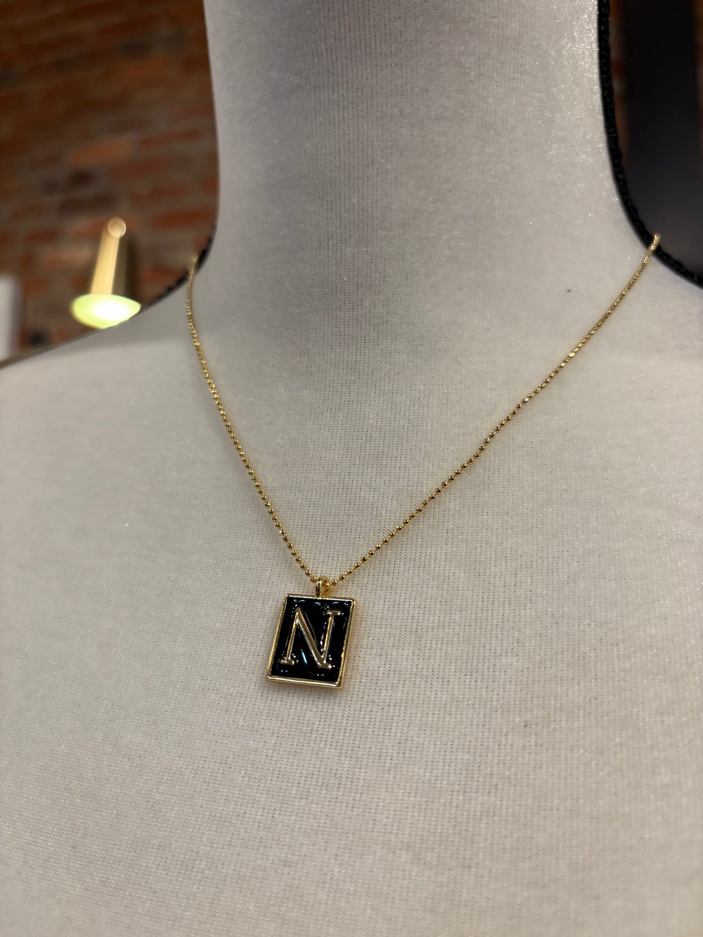 Necklace with a square pendant featuring the letter 'N' on a mannequin.