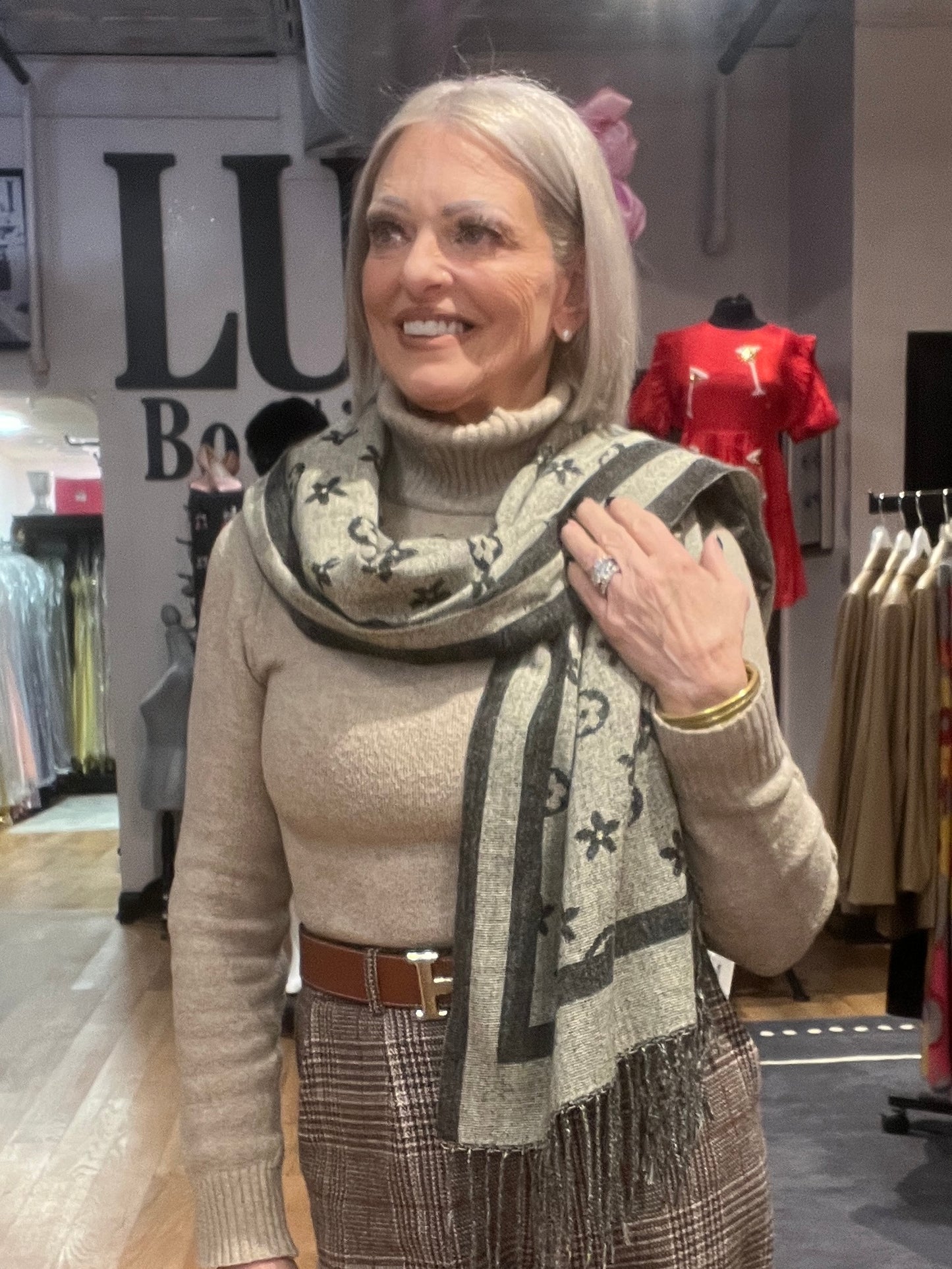 Woman wearing a beige sweater and patterned scarf in a clothing store.