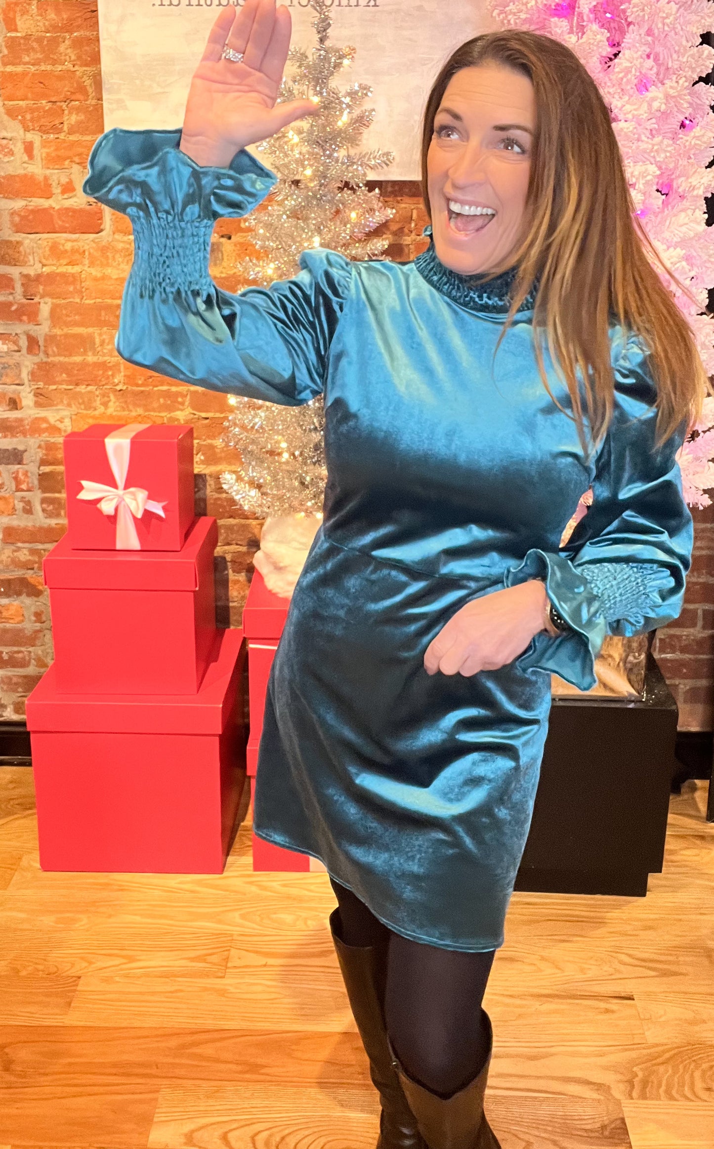 A woman wearing a teal velvet mini dress with a smocked neck and sleeves, paired with black tights and a pair of shoes.