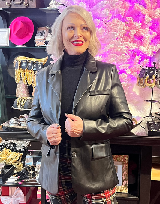 Woman in a store wearing a black leather jacket and plaid pants with a pink floral display in the background.