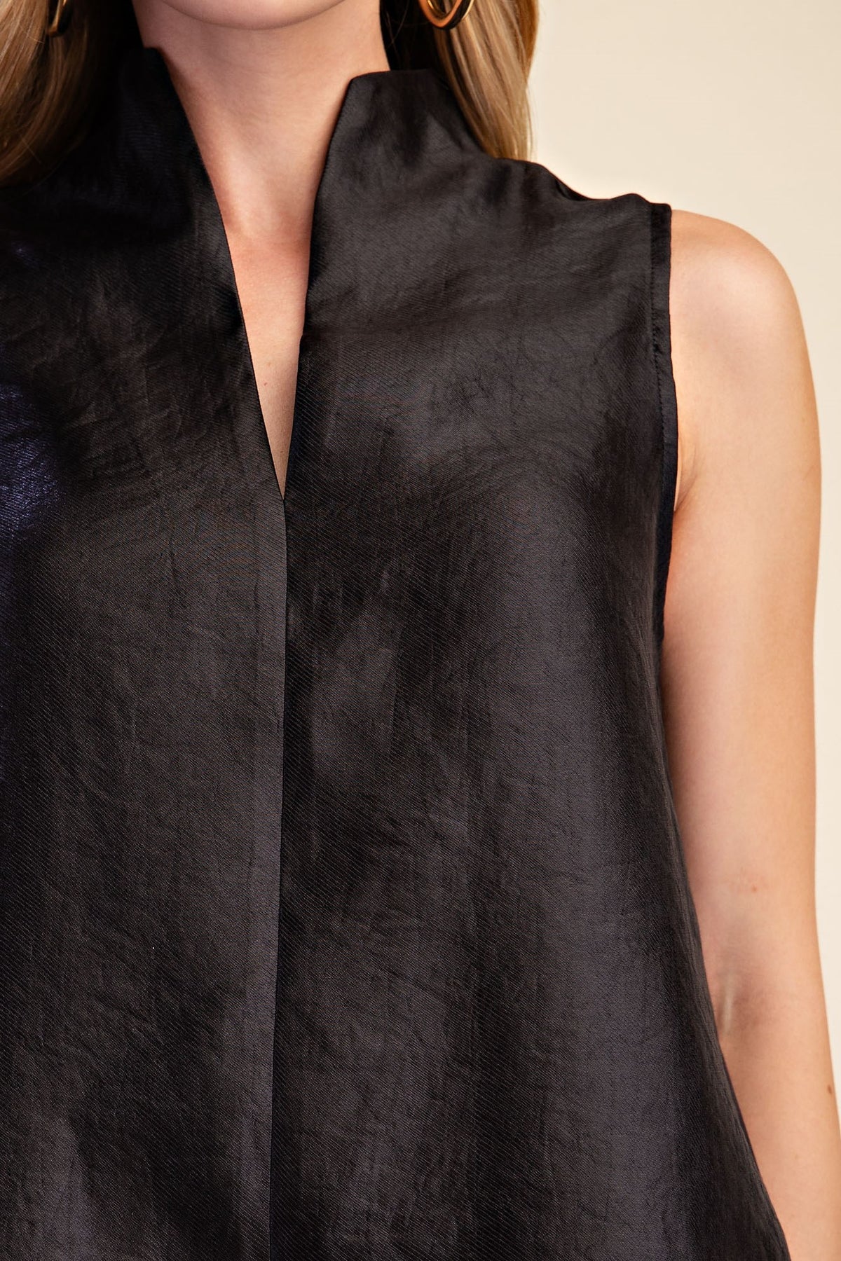 Close-up of a sleeveless black top with a high split neckline, worn by a model against a light beige background.