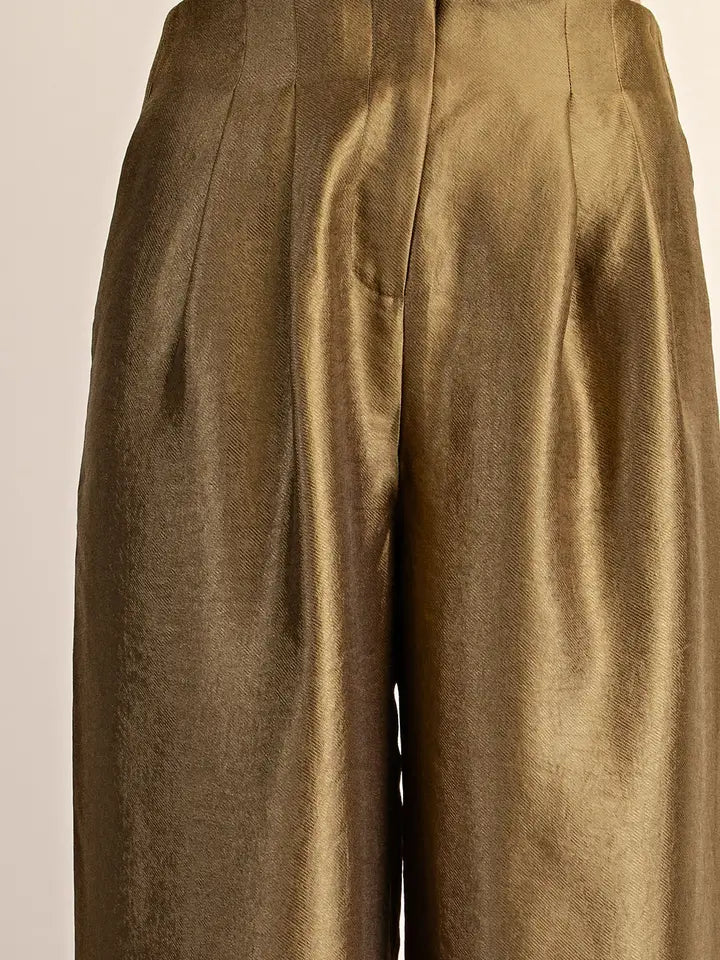 Close-up of high-waisted, wide-leg trousers in a metallic olive-gold fabric, showing the pleated front and satin-like sheen.