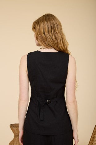 Woman wearing a black sleeveless dress with a belt against a beige background