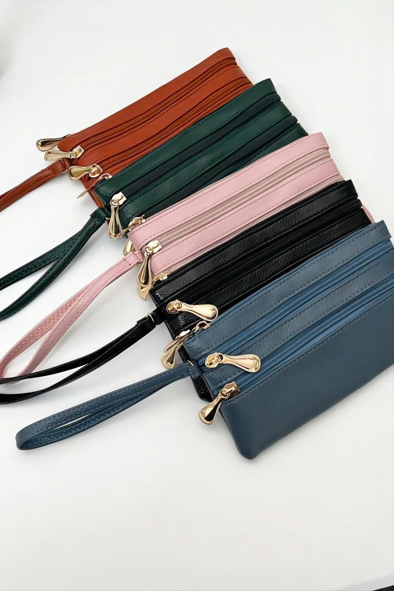 Five leather wristlet pouches with zippered closures and wrist straps, shown in brown, green, pink, black, and blue, arranged diagonally on a white background.