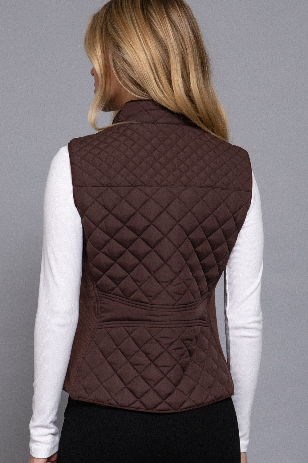 Person wearing a brown quilted vest on a gray background