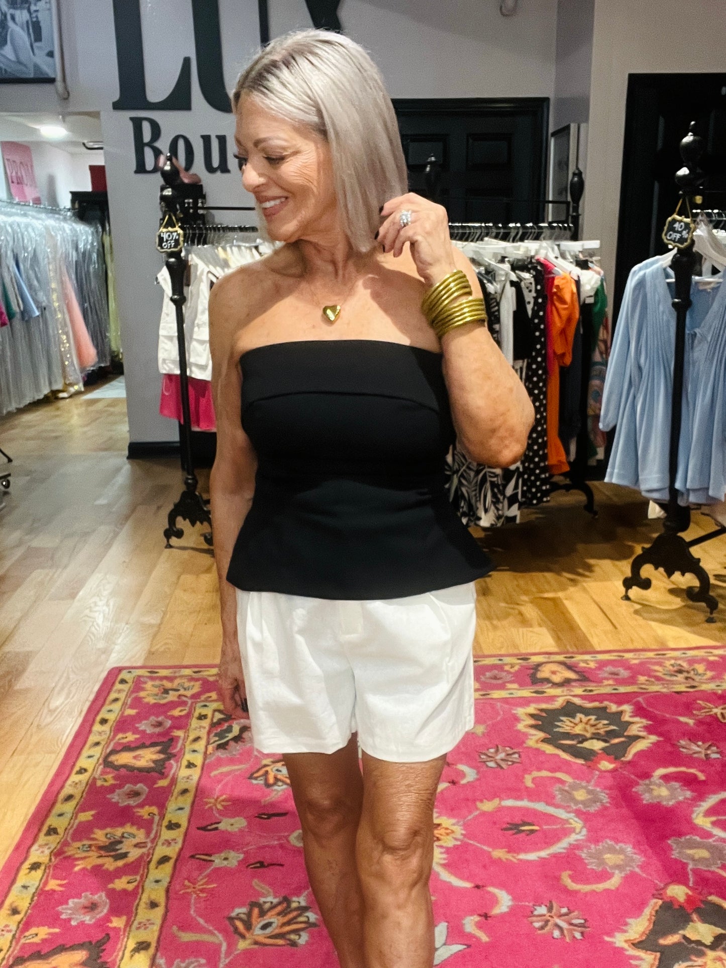 Woman in a black top and white shorts standing in a clothing store with racks of clothes in the background.