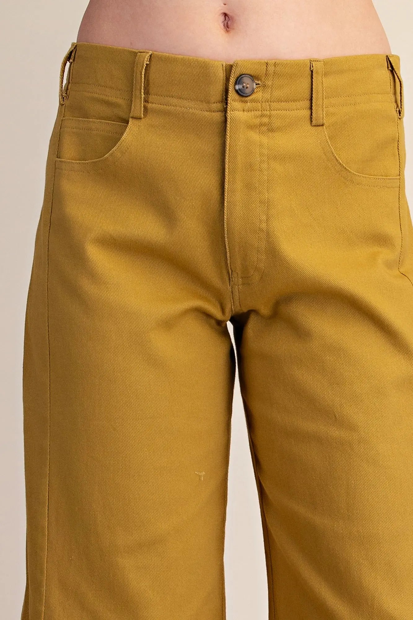 Close-up of a person wearing mustard yellow cropped pants, showing the waistband, button, front pockets, and upper legs against a plain light background.