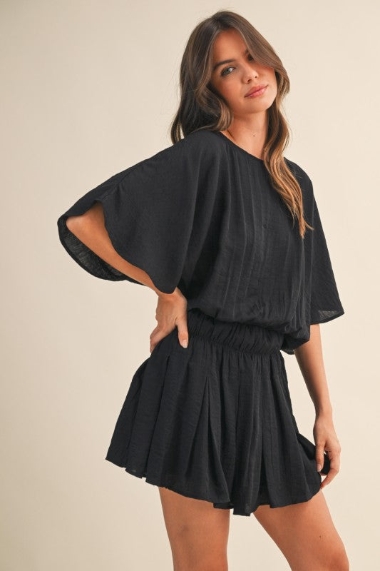 Woman wearing a black romper against a beige background