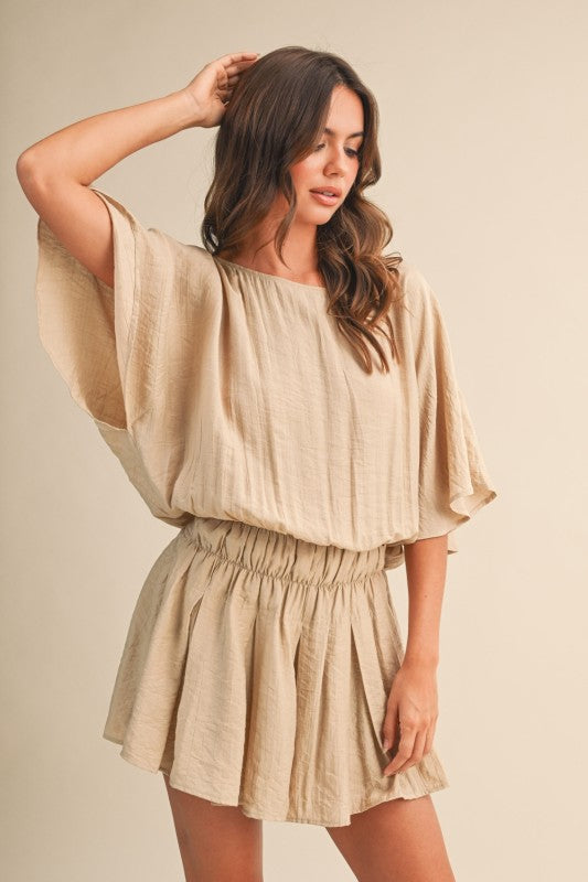 Woman wearing a beige romper against a plain background