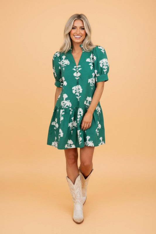 Woman wearing a green floral dress with white boots on a beige background