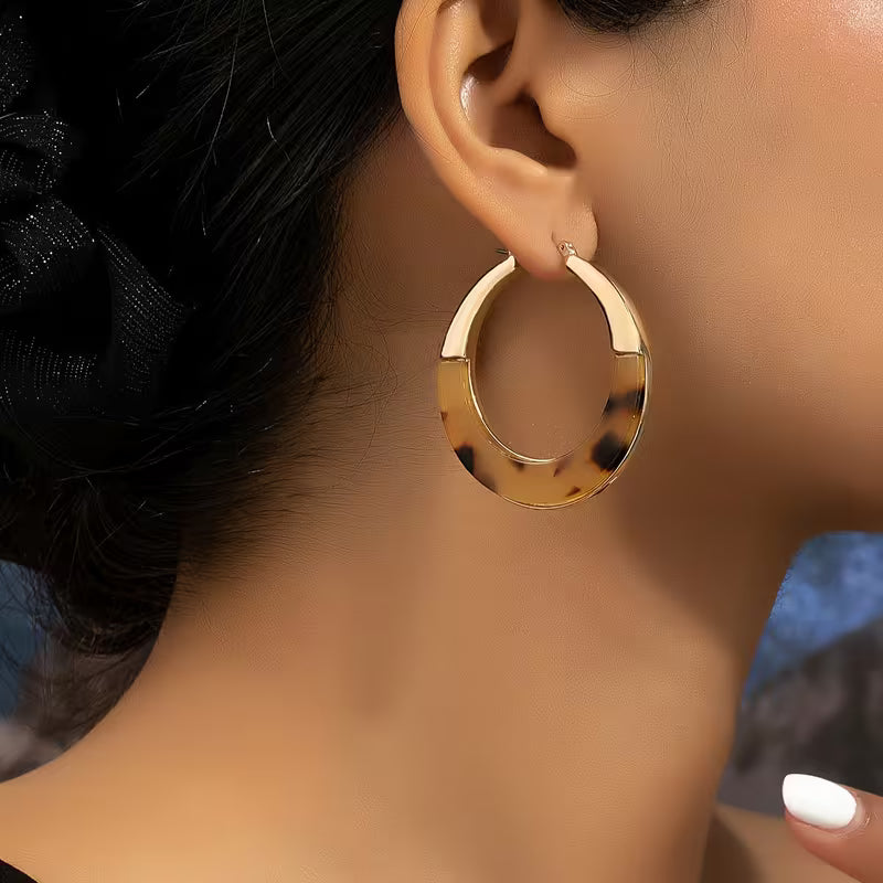 A close-up of a model's ear wearing a large gold hoop earring with a tortoiseshell pattern.