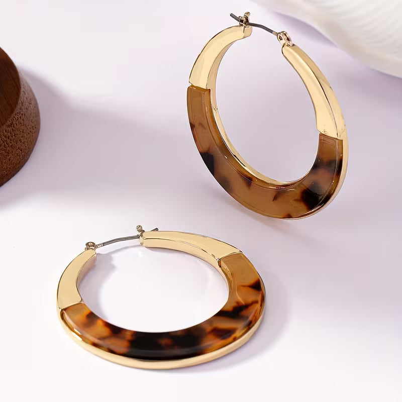 A pair of large hoop earrings with a gold-tone metal border and a brown tortoiseshell patterned center, displayed on a clean white surface.
