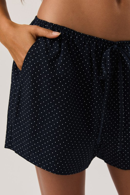 Navy blue shorts with white polka dots worn by a person on a neutral background
