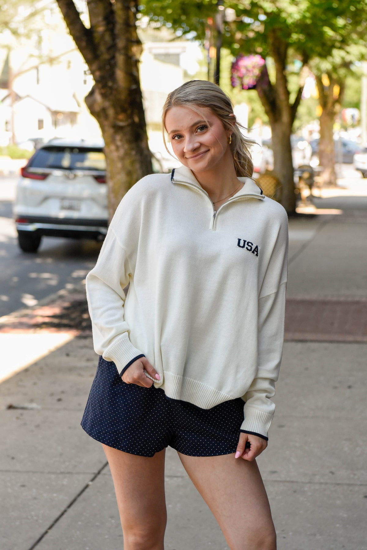 Woman wearing a white sweatshirt with 'USA' on it, standing on a sidewalk.