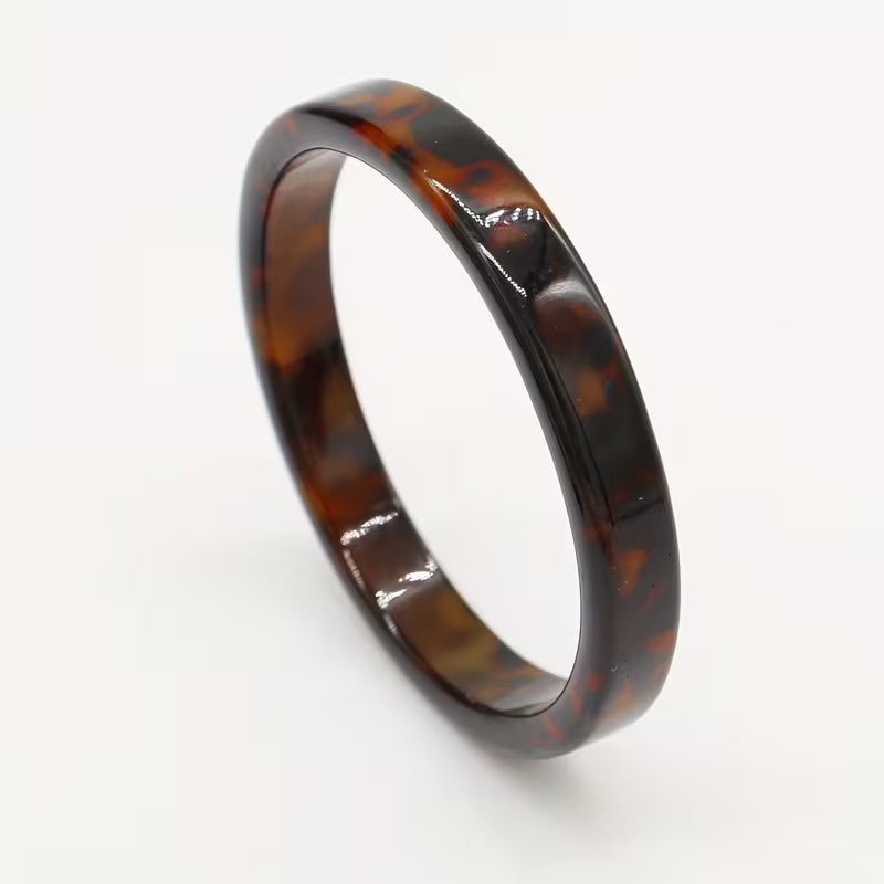 A glossy tortoiseshell ring with a dark brown and amber pattern, photographed on a clean white background.