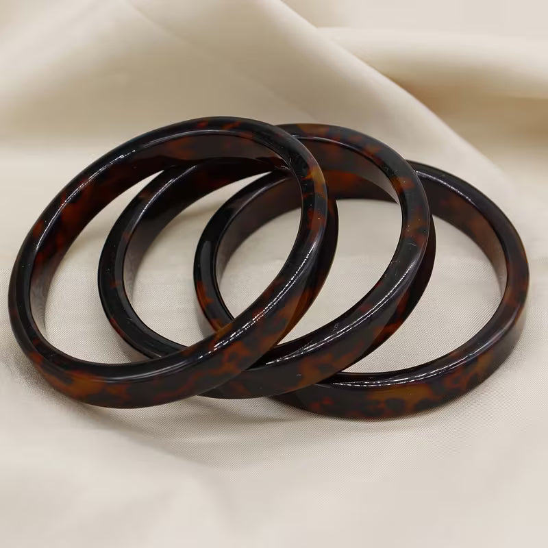 Three tortoiseshell bangles stacked together on a draped cream fabric background.