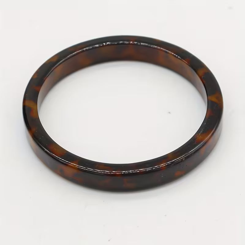 A glossy tortoiseshell bangle bracelet in dark brown and amber tones, photographed on a plain white background.