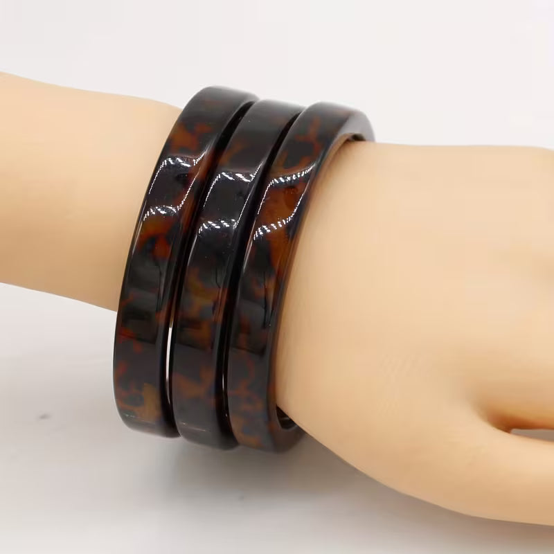 Three stacked glossy tortoiseshell bangles displayed on a beige mannequin wrist against a plain white background.
