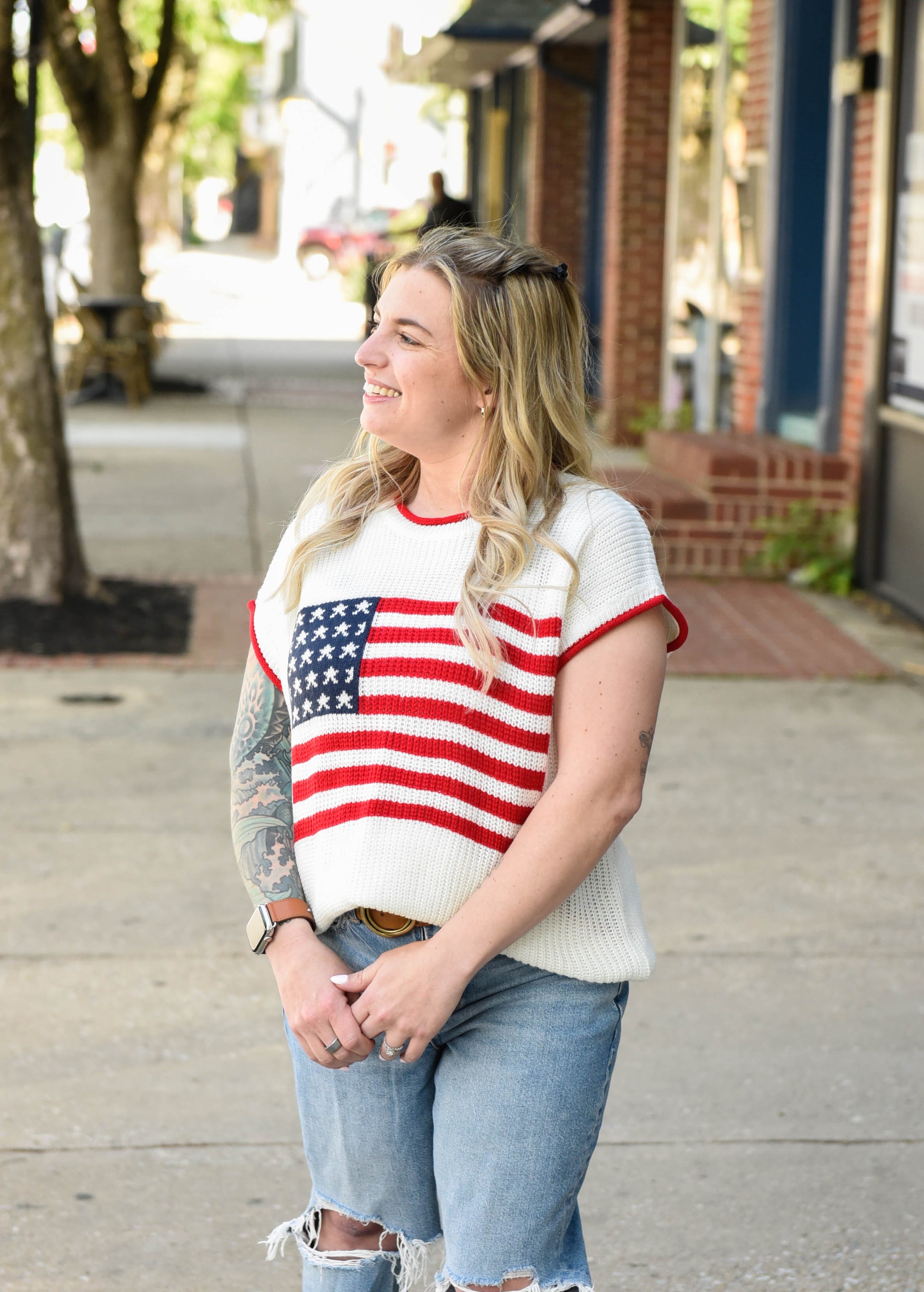 Woman wearing a sweater with an American flag design on a city street.