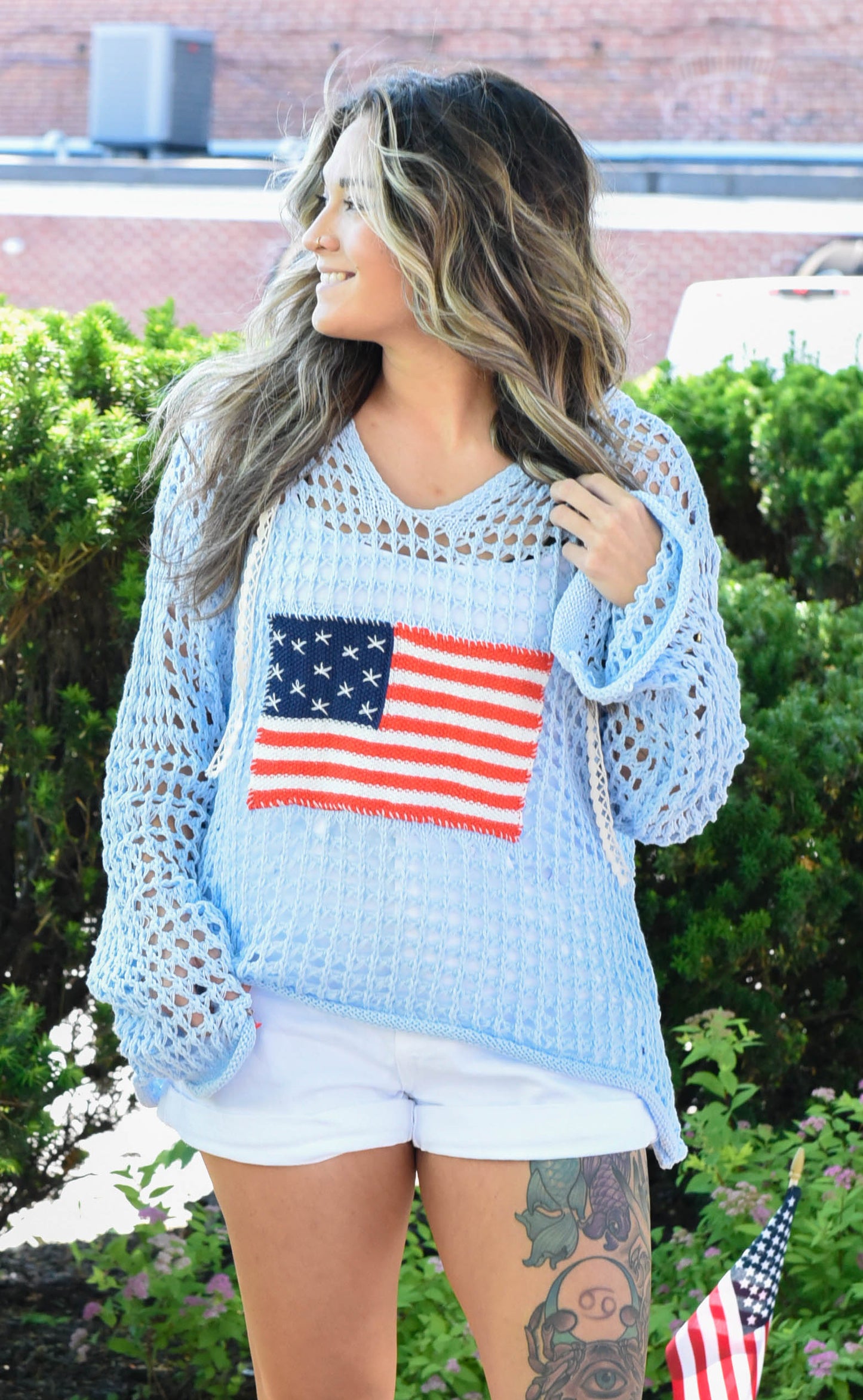 Woman wearing a light blue sweater with an American flag design outdoors.