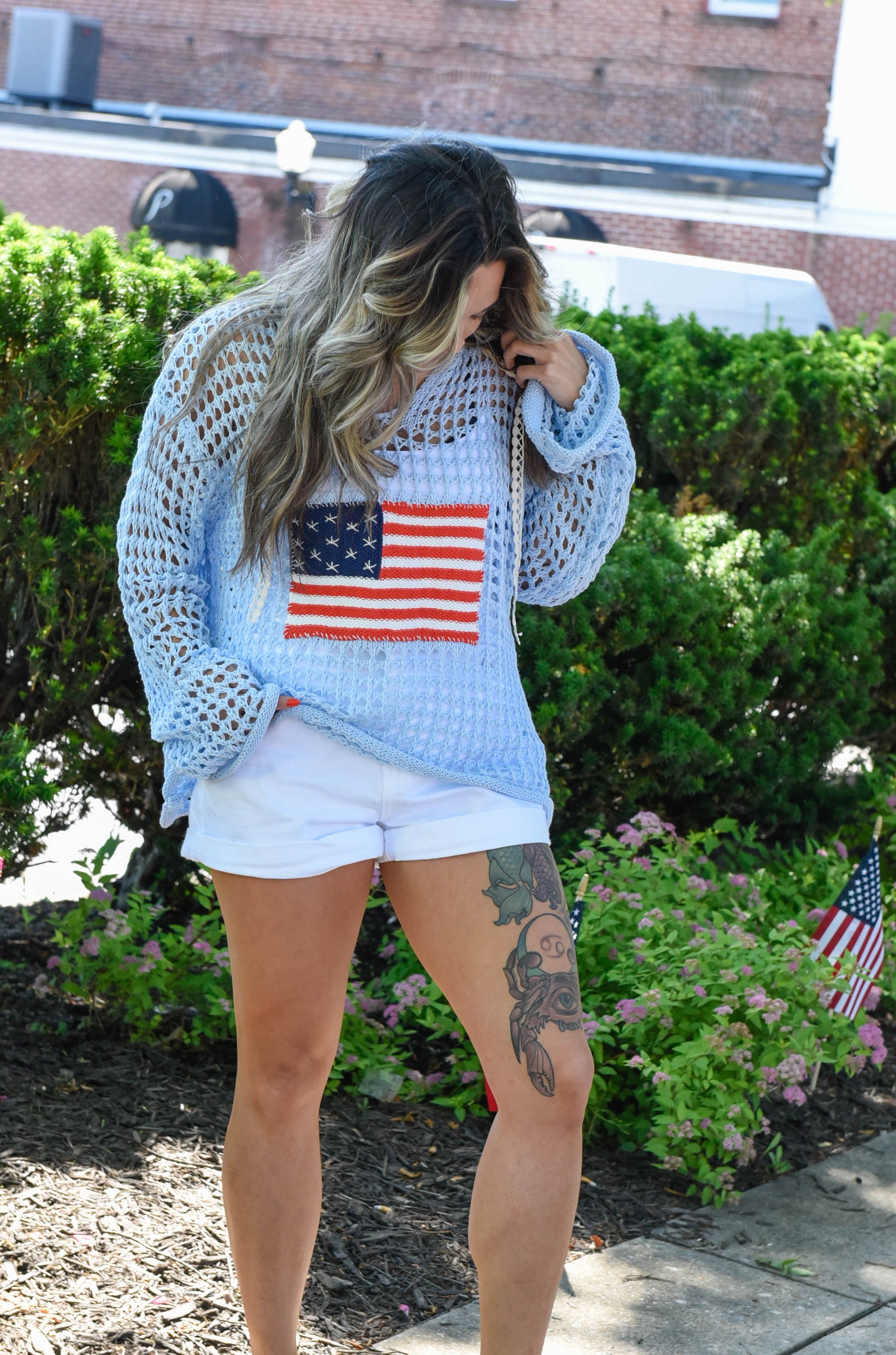 Woman wearing a light blue sweater with an American flag design outdoors.