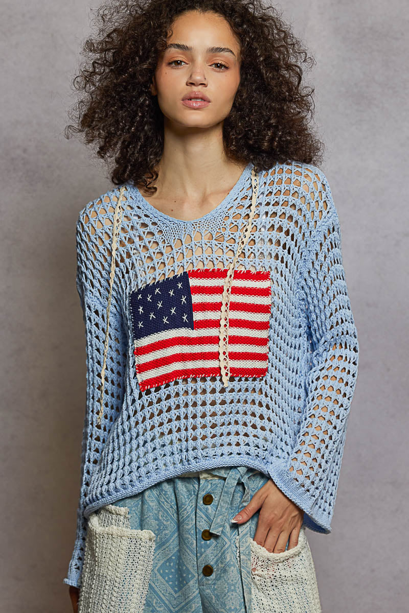 Woman wearing a blue crochet sweater with an American flag design against a gray background