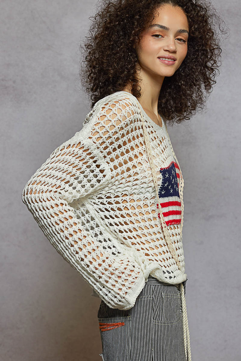 Woman wearing a white crochet sweater with an American flag patch against a gray background