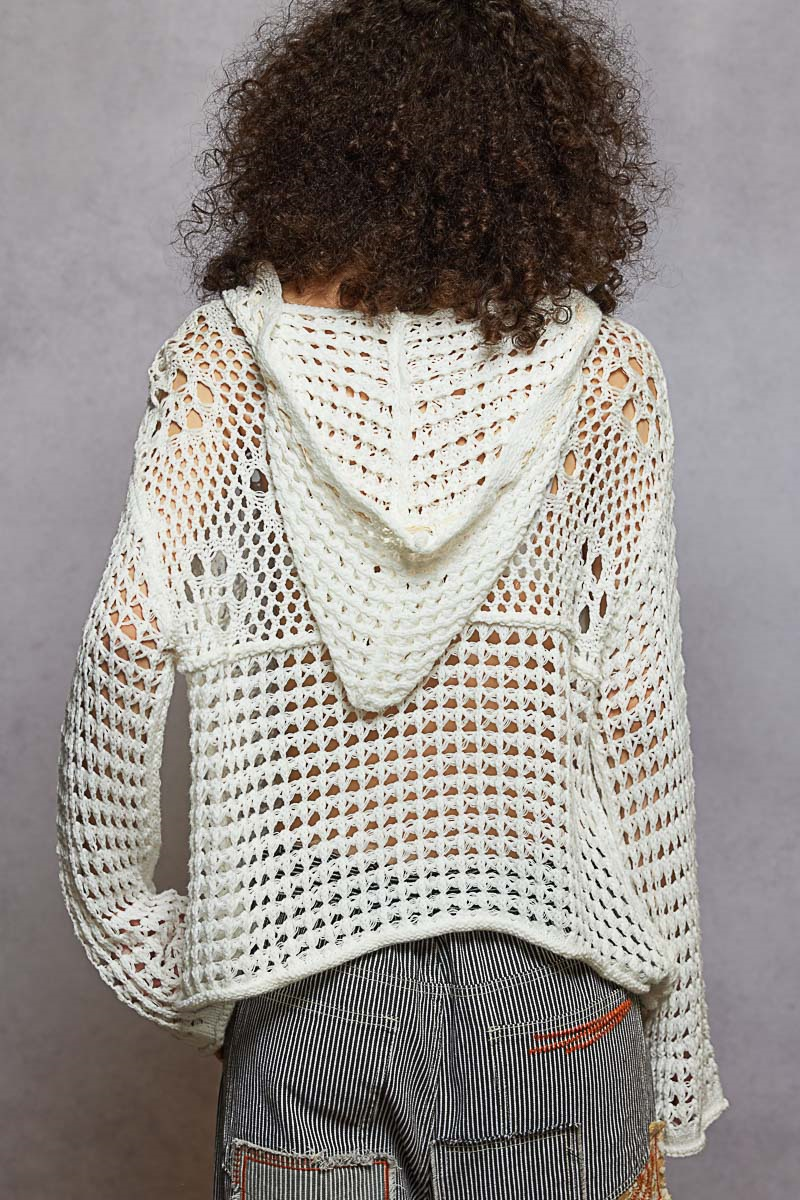 Person wearing a white crochet hoodie against a gray background