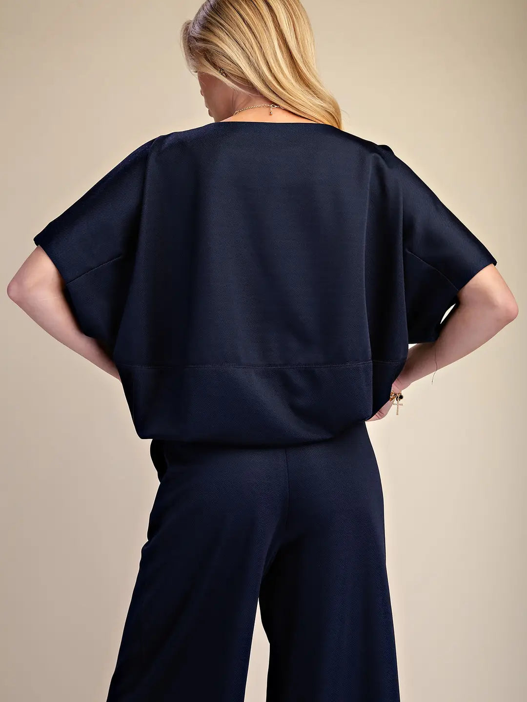 A woman shown from the back wearing a dark navy blue short-sleeve top and matching wide-leg trousers against a plain beige studio background.