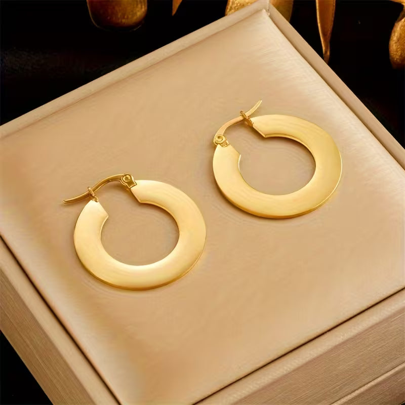 A pair of chunky gold hoop earrings displayed on a beige jewelry box.