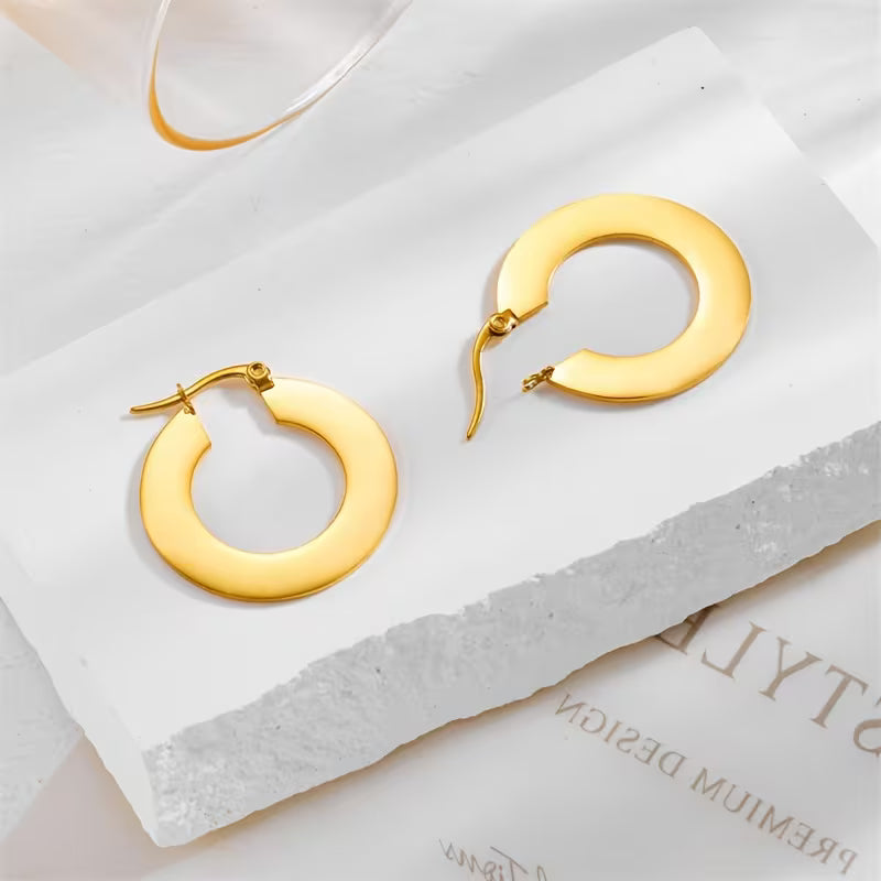 Gold hoop earrings on a white surface with a branded box in the background