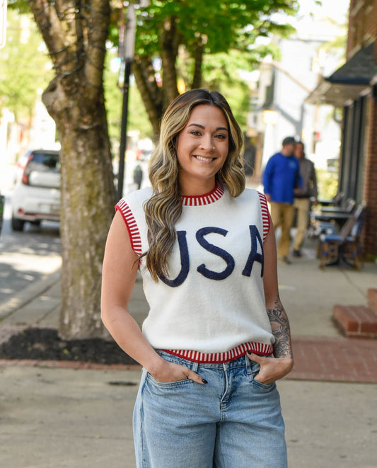 Woman wearing a sleeveless shirt with 'USA' on it, standing outdoors.