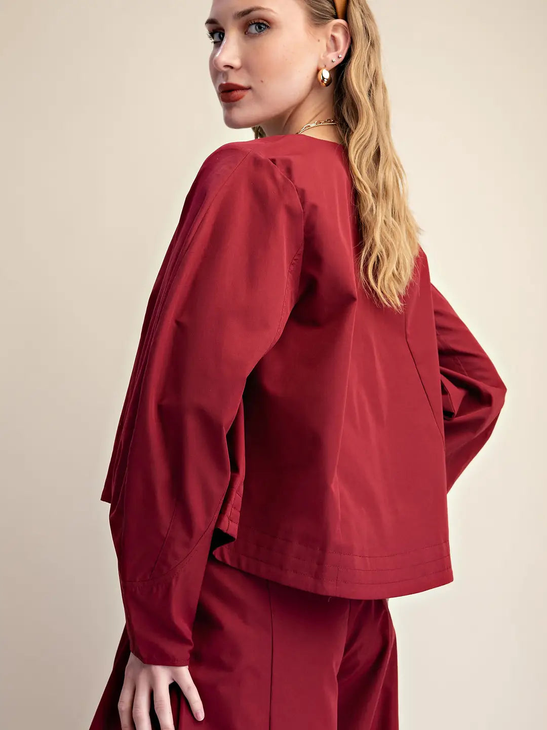 A woman wearing a matching burgundy scrub top and scrub pants, photographed from the back and side against a plain beige studio background.