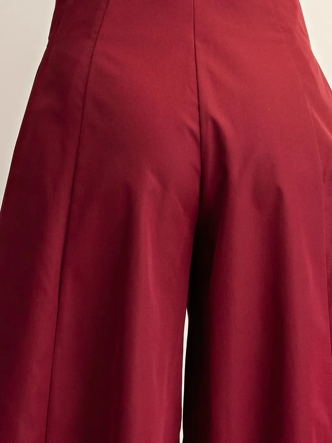 Close-up of a pair of high-waisted, wide-leg trousers in a deep burgundy red fabric, showing the front center seam and pleated texture.