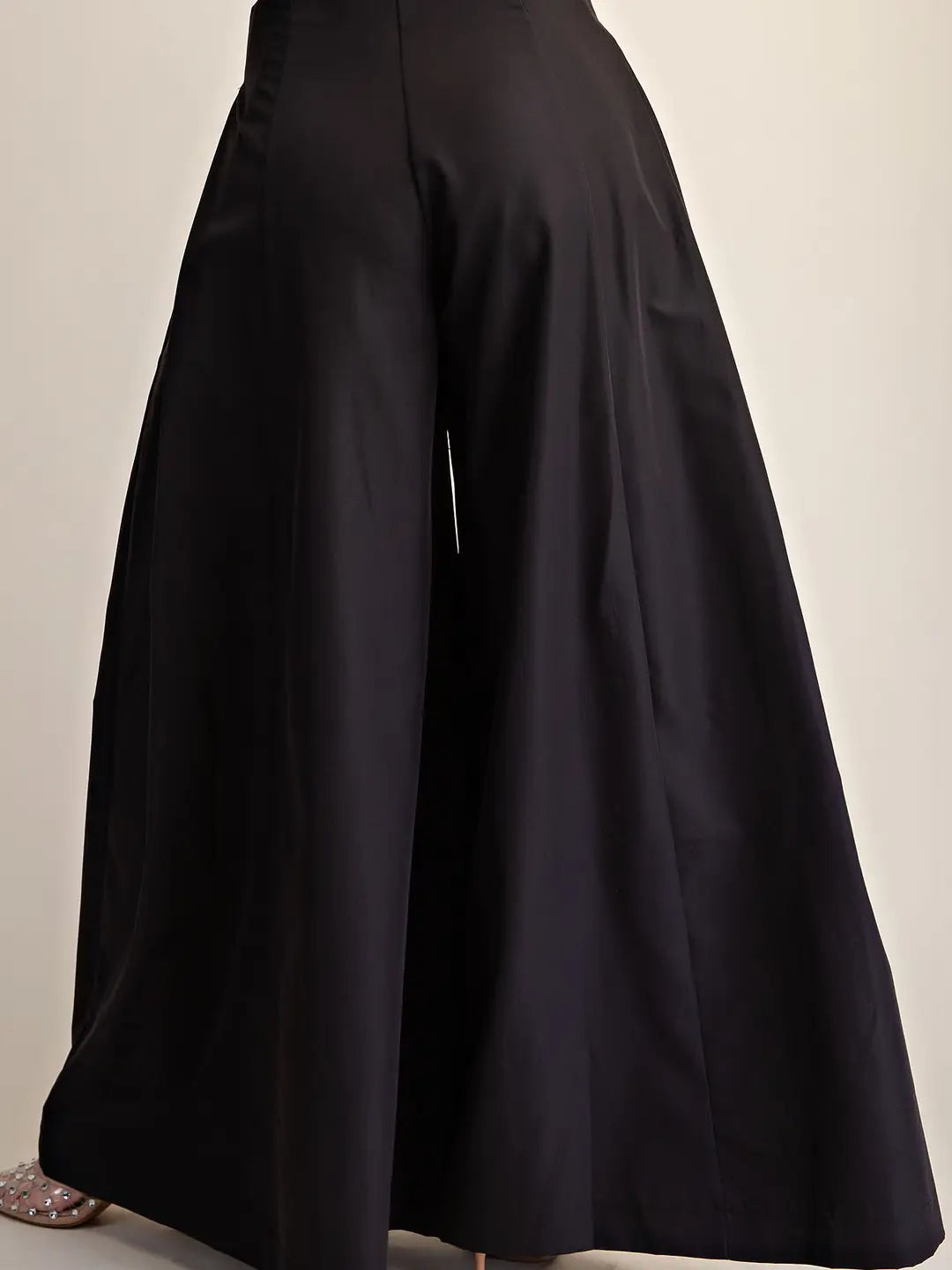 Black wide-leg cropped pants shown from the back, featuring a high waist and a dramatic flared silhouette, photographed against a plain light background.