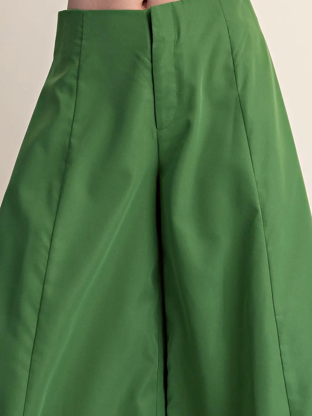 Close-up of a person wearing bright green wide-leg cropped pants, showing the front center seam and fabric drape against a plain light background.