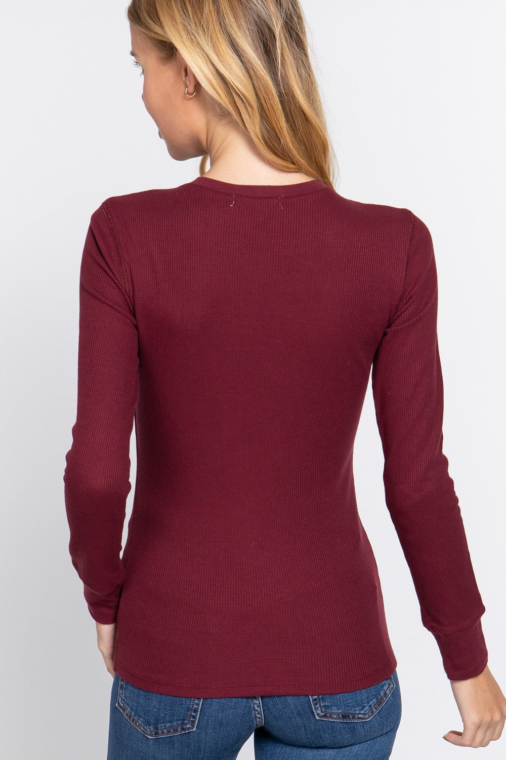 A woman shown from the back wearing a fitted long-sleeve ribbed knit top in burgundy, paired with blue jeans, against a plain light gray studio background.