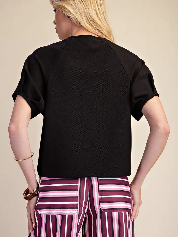 A woman shown from the back wearing a black short-sleeve crop top and pink, purple, and white striped pants, set against a plain beige studio background.
