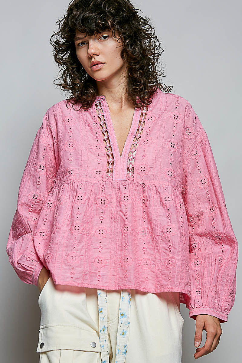 Person wearing a pink embroidered blouse with white pants against a gray background