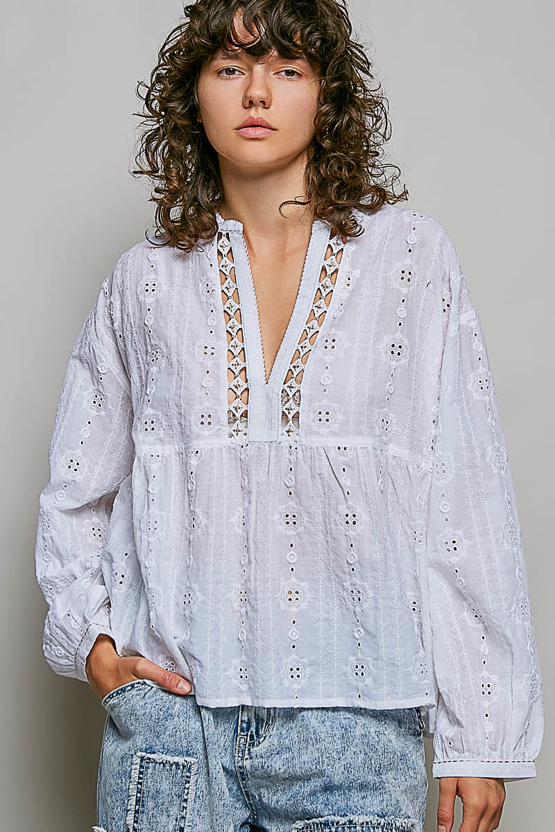 Person wearing a white embroidered blouse with a gray background