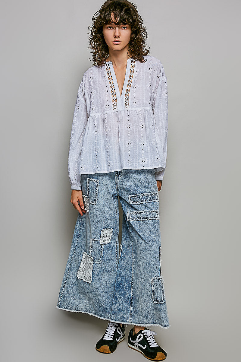 Person wearing a light blue embroidered top and denim cargo pants on a gray background