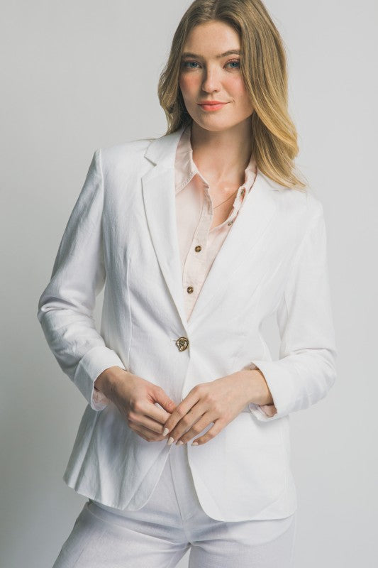 Woman wearing a white suit with a light pink shirt on a plain background