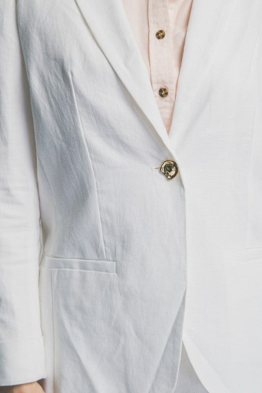 Close-up of a light gray blazer with a button and part of a pink shirt visible.