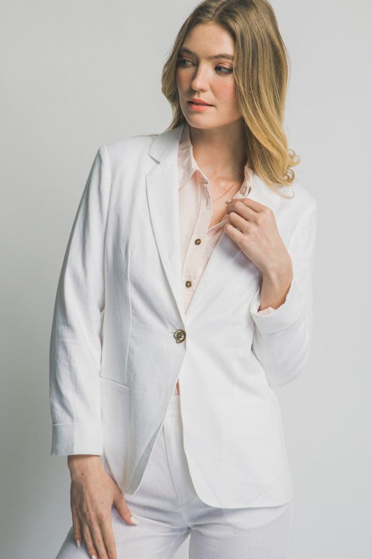 Woman wearing a white blazer over a light pink shirt on a plain background