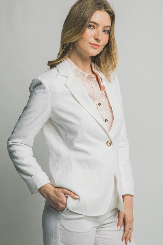 Woman wearing a white blazer over a light pink top on a plain background