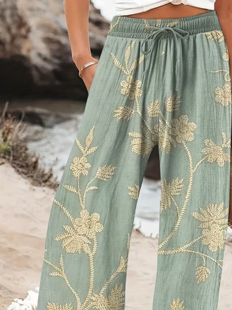 Green pants with gold floral patterns worn by a person on a beach.