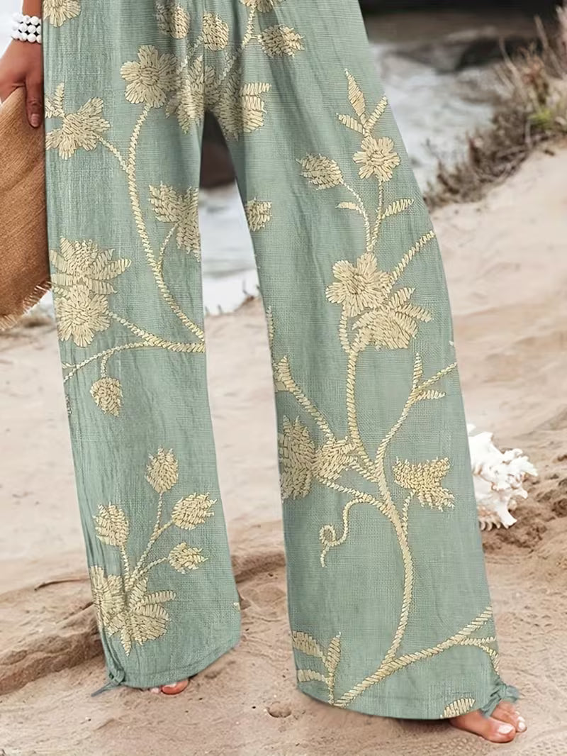 Green pants with gold floral embroidery worn by a person on a sandy surface.
