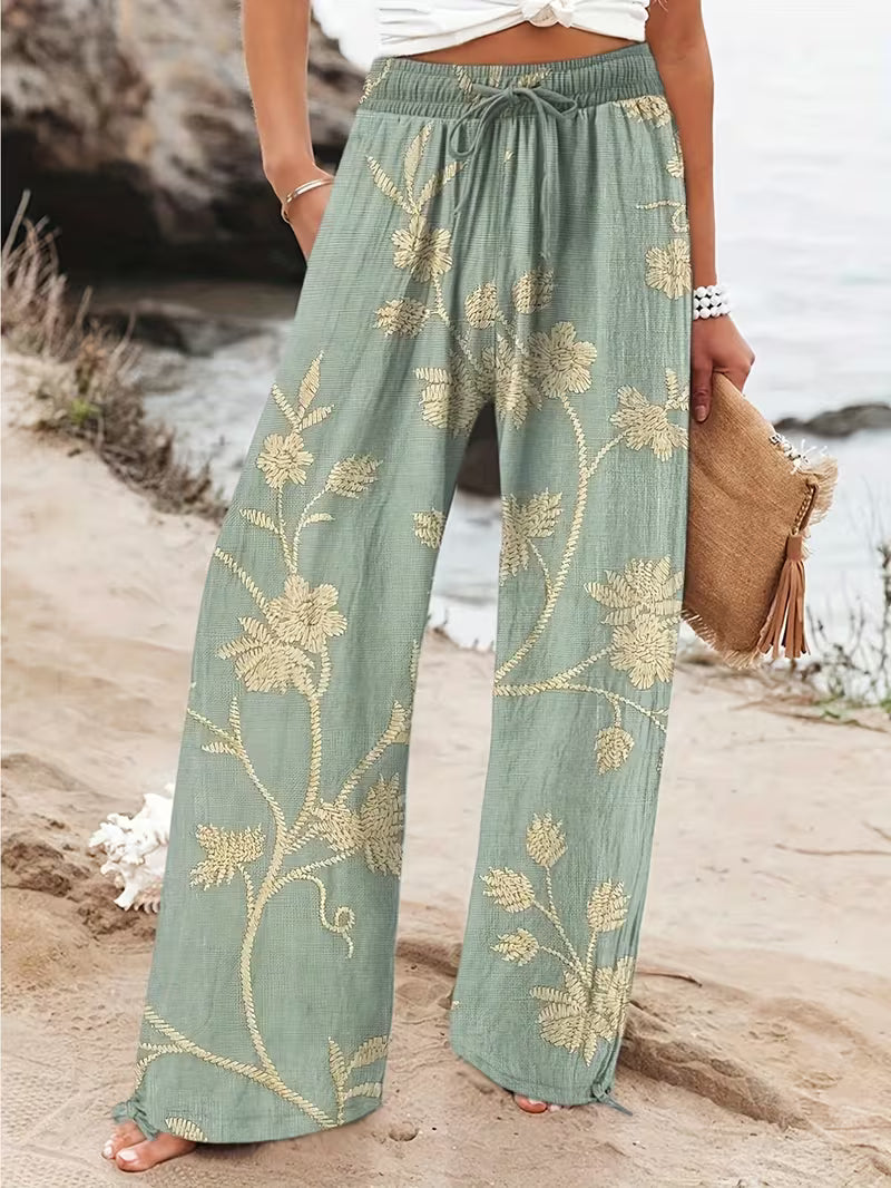 Person wearing green floral-patterned pants by a rocky shoreline.